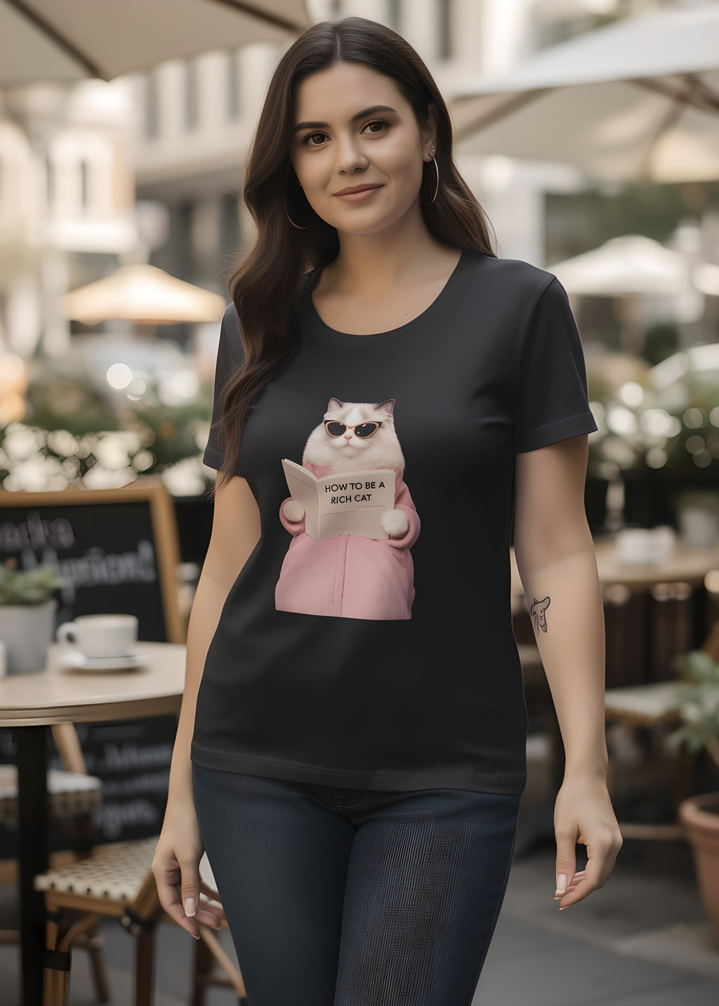 Woman wearing a black t-shirt featuring a cool cat reading How to be a Rich Cat. Outdoor cafe setting.