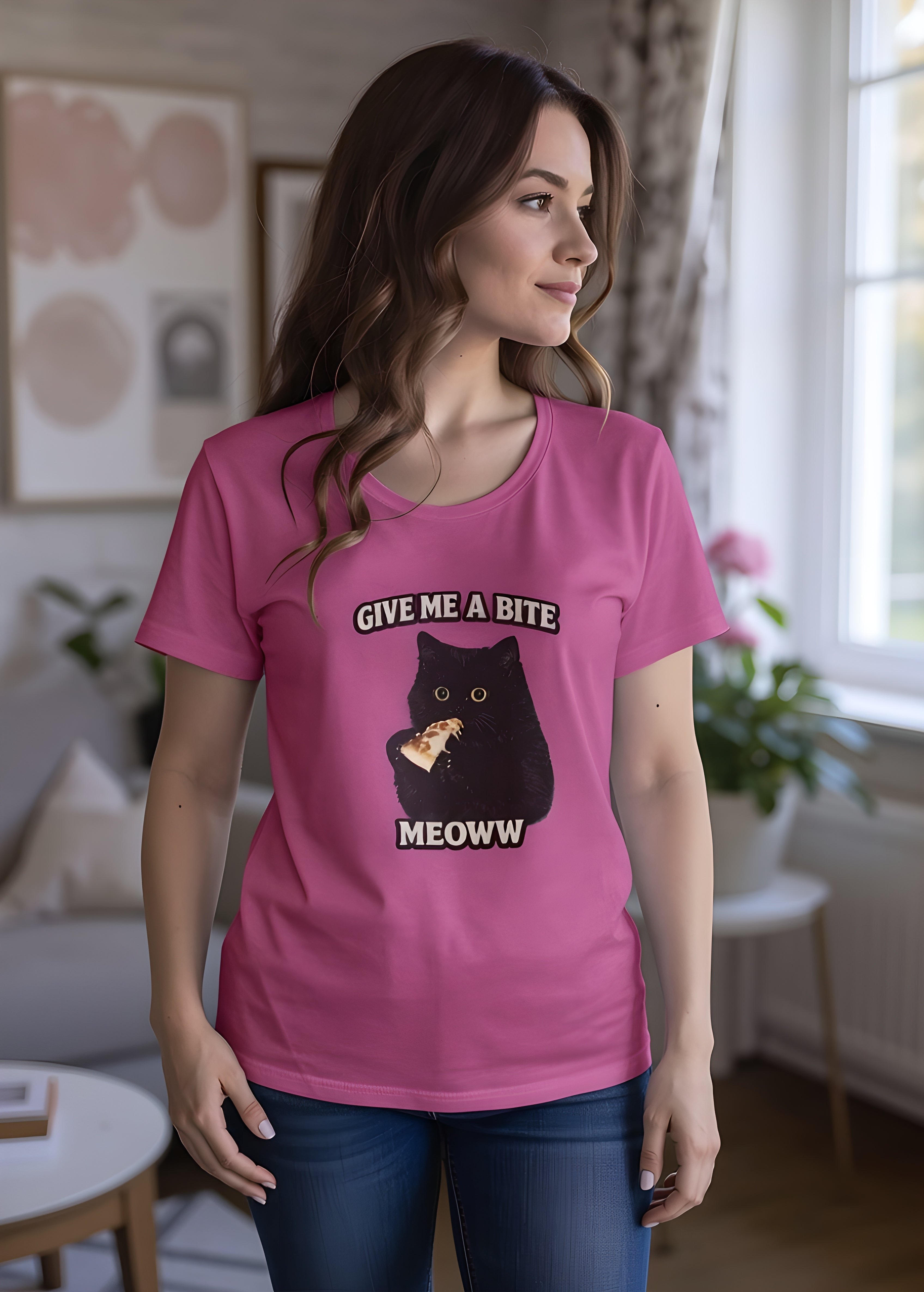 Woman wearing a pink t-shirt featuring a whimsical cat graphic and the text Give me a bite Meoww.